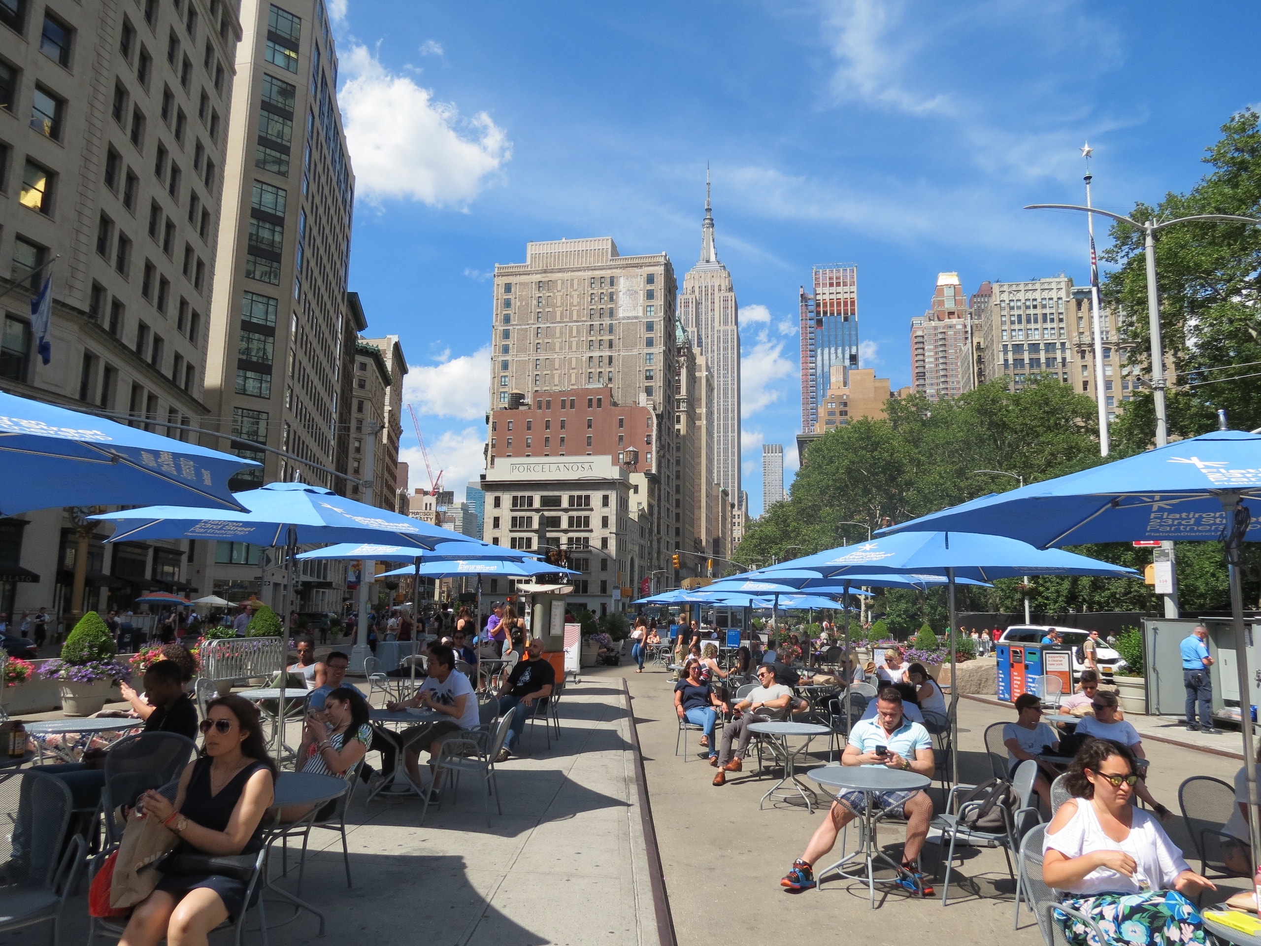 Blue umbrellas shade people sitting at tables and chairs throughout the North Flatiron Plaza